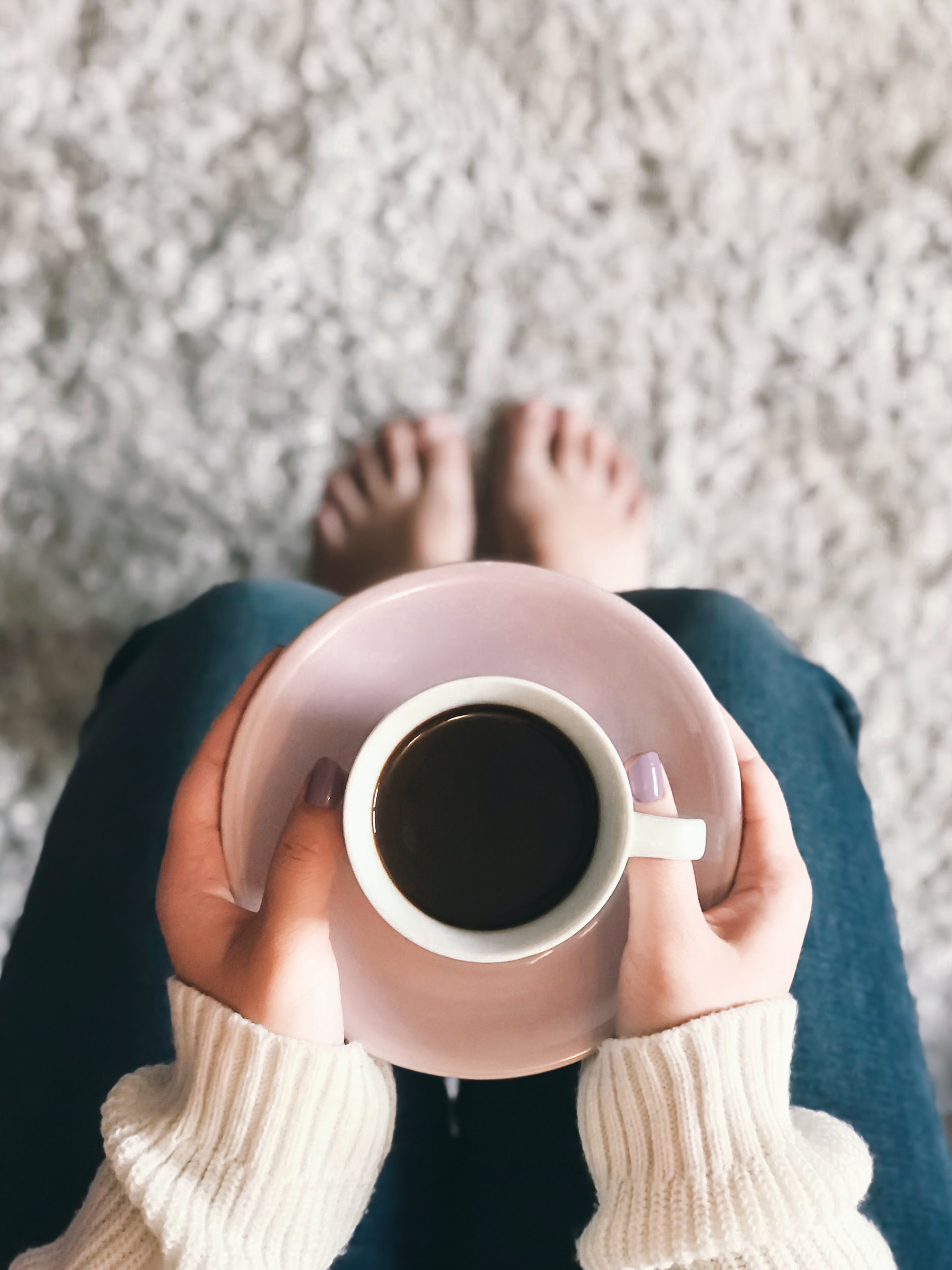 chica con taza de café apoyada en las rodillas con una alfombra blanca de fondo vista desde arriba